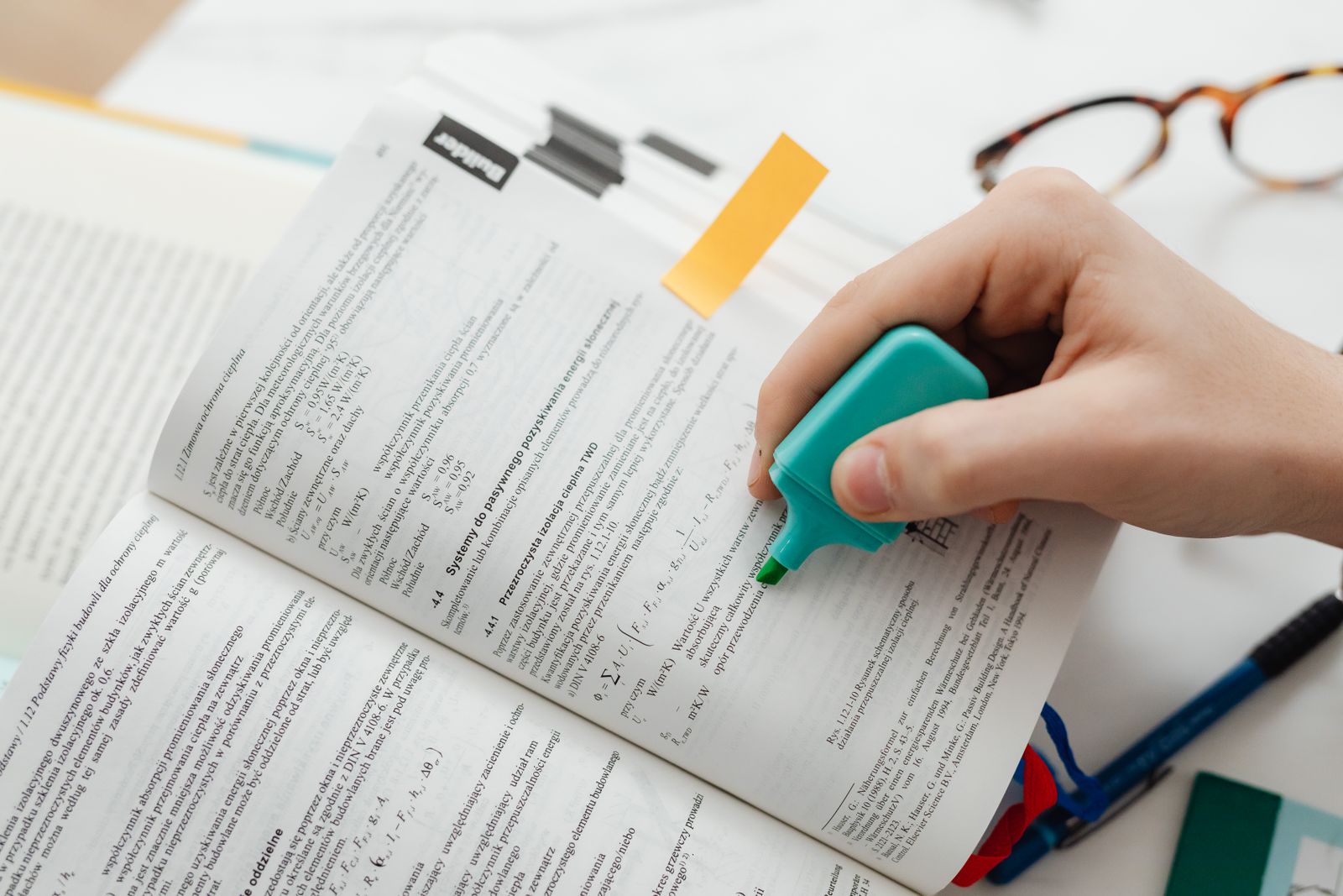 Close-up of a hand using a highlighter to mark key information in a textbook
